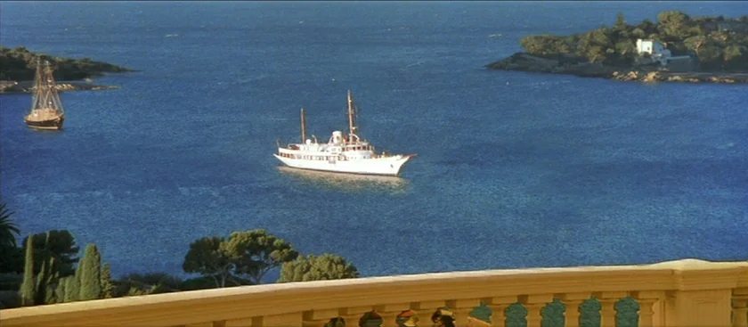 The House of Mirth (2000) movie still: establishing — A tranquil Mediterranean bay with deep blue water framed by a beige stone balustrade. A white…