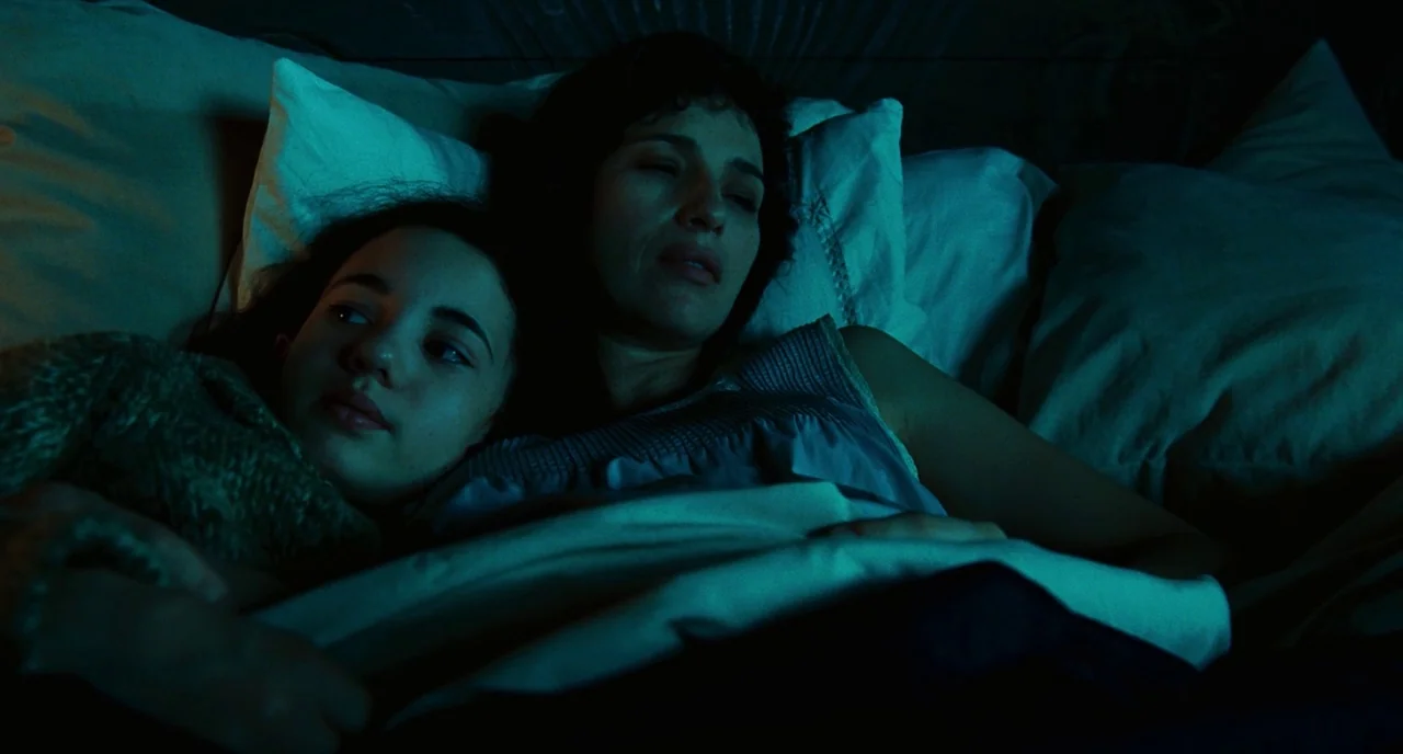 Pan’s Labyrinth (2006) movie still: medium — A dark room with two people resting on a bed covered in pillows. They lay side by side under a sheet in…