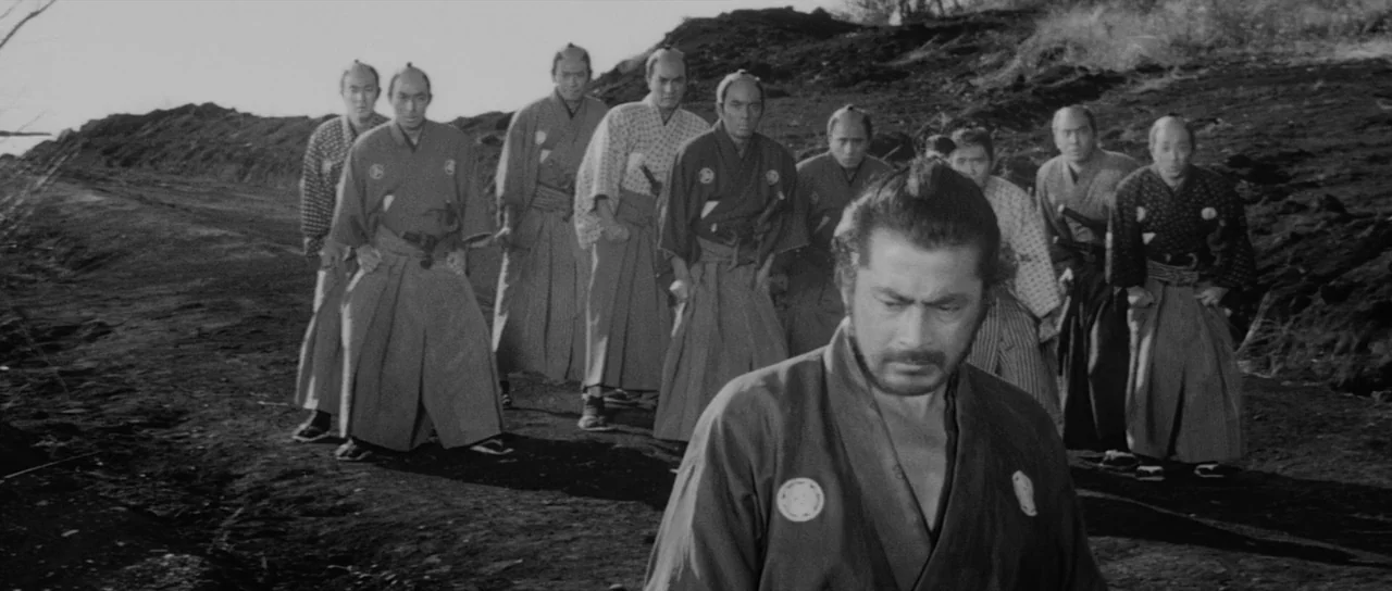Sanjuro (1962) movie still: fullbody — A group of men in traditional Japanese robes walk across a barren dirt landscape. The foreground man leads…