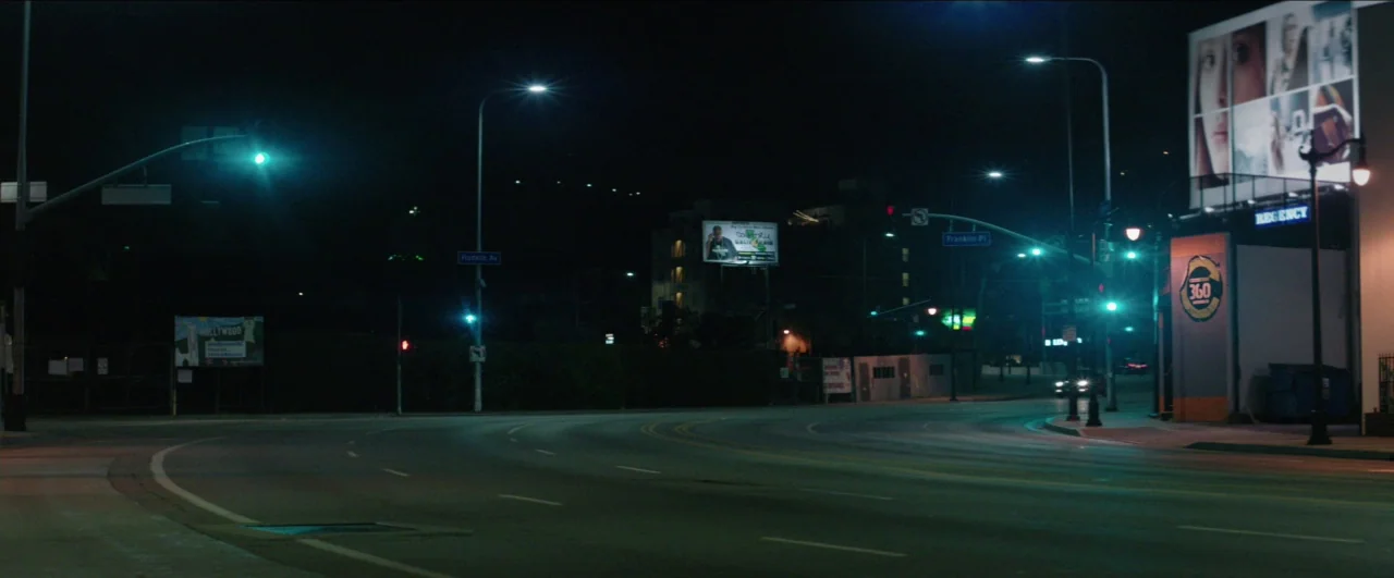 Dean (2016) movie still: establishing — An empty urban intersection at night features multiple streetlamps illuminating the curving asphalt road.…