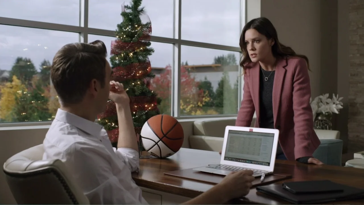 Always and Forever Christmas (2019) movie still: medium — An office space features a large window, a Christmas tree, and a wooden desk. A woman…