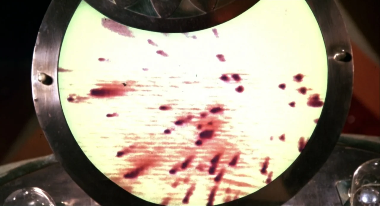 Hercules (1983) movie still: closeup — A close-up view shows a circular device screen with dark spots on a pale background. The metal-rimmed…