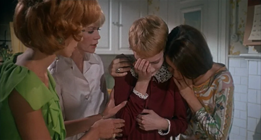 Rosemary’s Baby (1968) movie still: medium — Four women stand in a 1960s interior space with white cabinetry in the background. Three women surround…