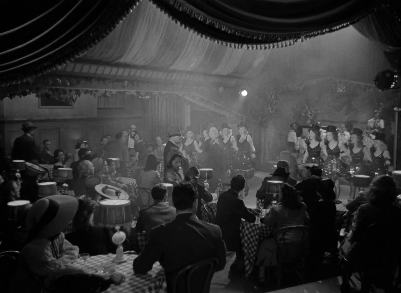 Dance, Girl, Dance (1940) movie still: wide — A dimly lit 1940s nightclub features checkered tablecloths and a small stage for performers. Several…