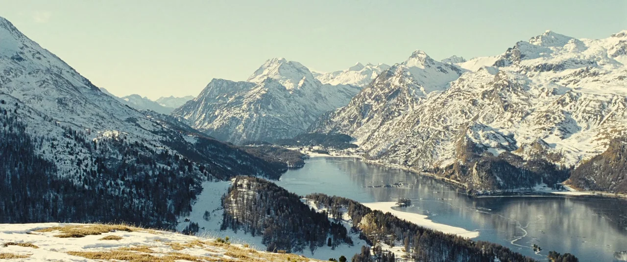 Clouds of Sils Maria (2014) movie still: establishing — A wide mountain valley features a large lake surrounded by snow-covered peaks and forests.…