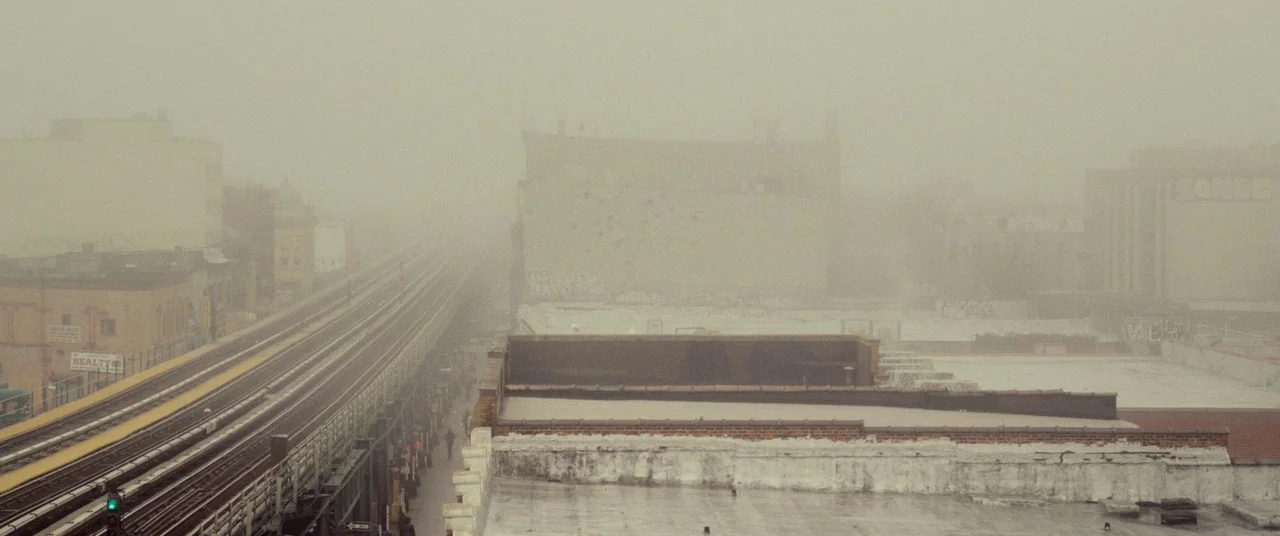 I Origins (2014) movie still: establishing — An elevated subway line runs through a dense, foggy cityscape of urban rooftops. The tracks stretch…