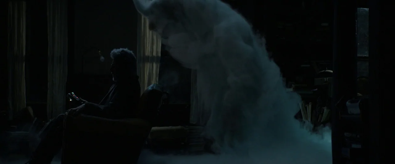 Ghostbusters: Afterlife (2021) movie still: medium — A dimly lit room with bookshelves and curtains is filled with swirling ethereal mist. A man…