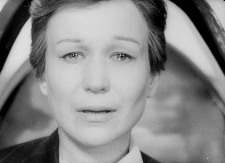 Wings (1966) movie still: closeup — A close-up shot of a person indoors against an out-of-focus background. A woman with short dark hair stares into…