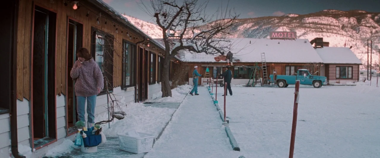 The Sweet Hereafter (1997) movie still: wide — A snowy motel exterior with wooden walls and a mountain range in the distance. A woman stands in a…