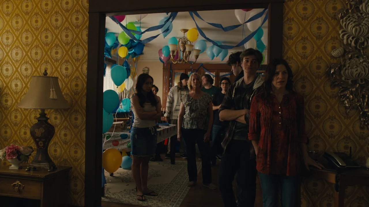Cam (2018) movie still: wide — A decorated living room contains many colored balloons and streamers hanging from the ceiling. A small group of…