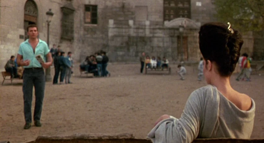 Matador (1986) movie still: medium — An outdoor paved plaza with stone walls and architectural details in the background. A man stands in the middle…