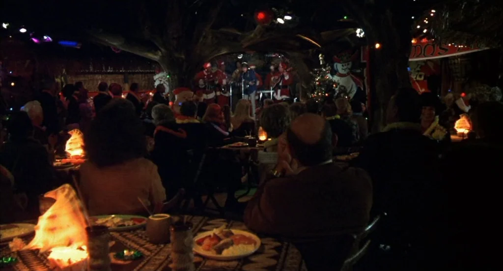 Melvin & Howard (1980) movie still: wide — A dimly lit tiki-themed venue features patrons seated at tables facing a musical stage. A band performs…