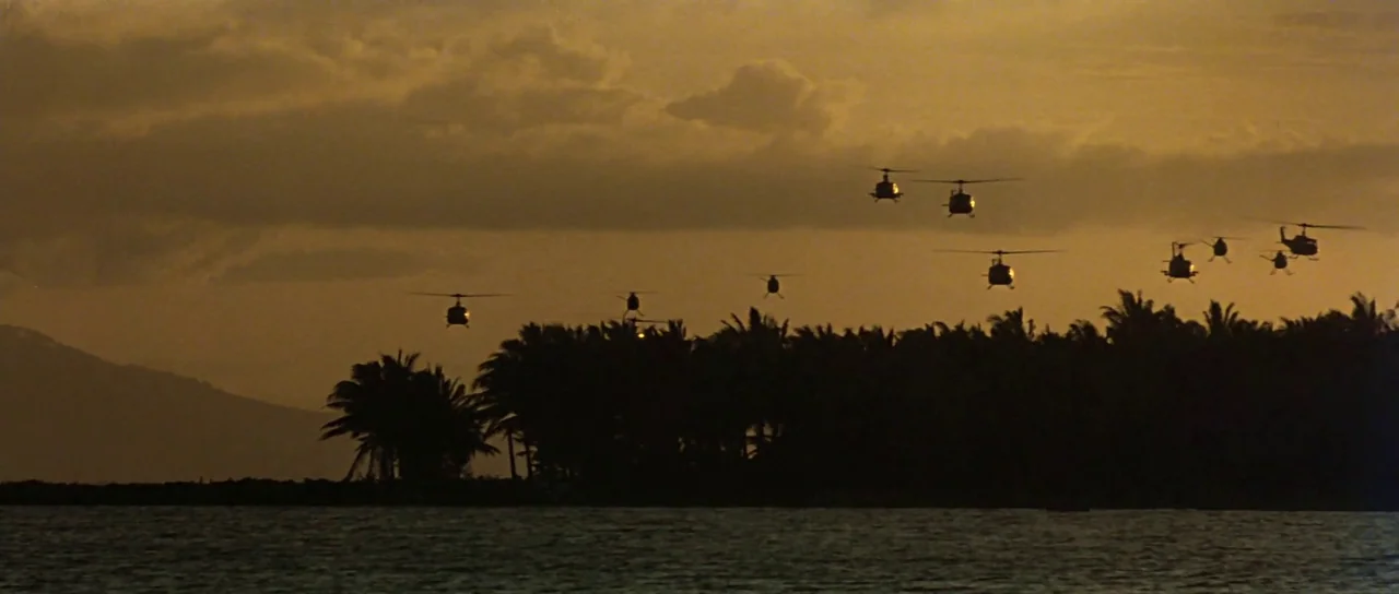 Apocalypse Now (1979) movie still: wide — A group of military helicopters flies in formation over a dense tropical treeline. The scene is…