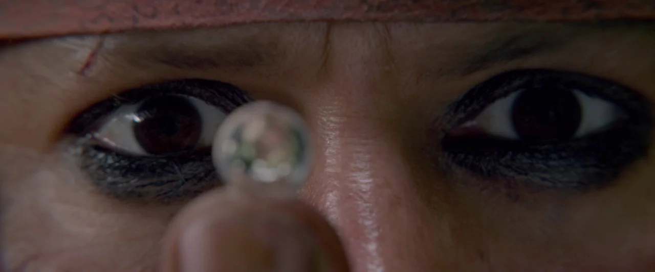 Pirates of the Caribbean: On Stranger Tides movie still: closeup — A close-up captures a person's eyes and forehead in low light. A small spherical…