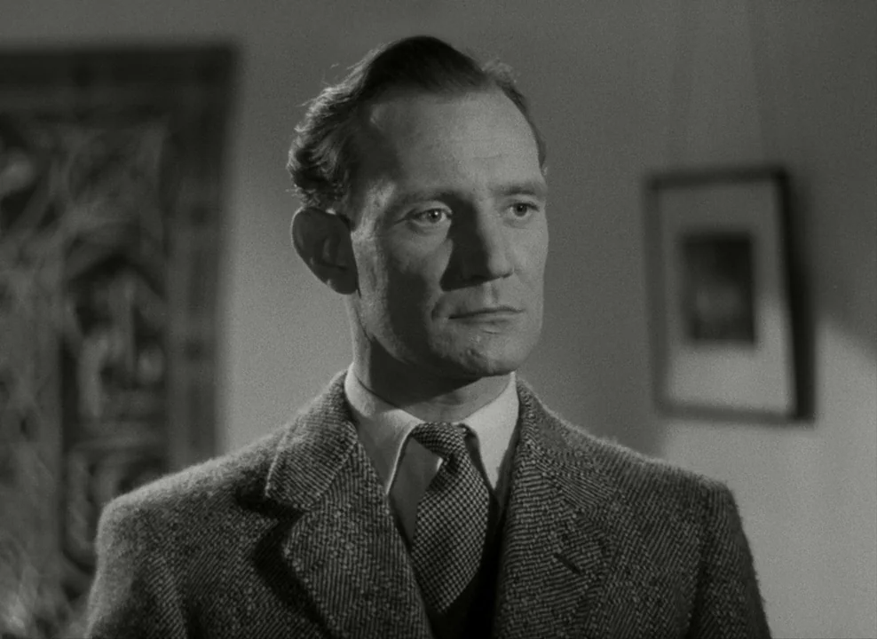Brief Encounter (1945) movie still: medium — A man stands inside a room with a framed artwork on the back wall. The man stares directly off-camera…