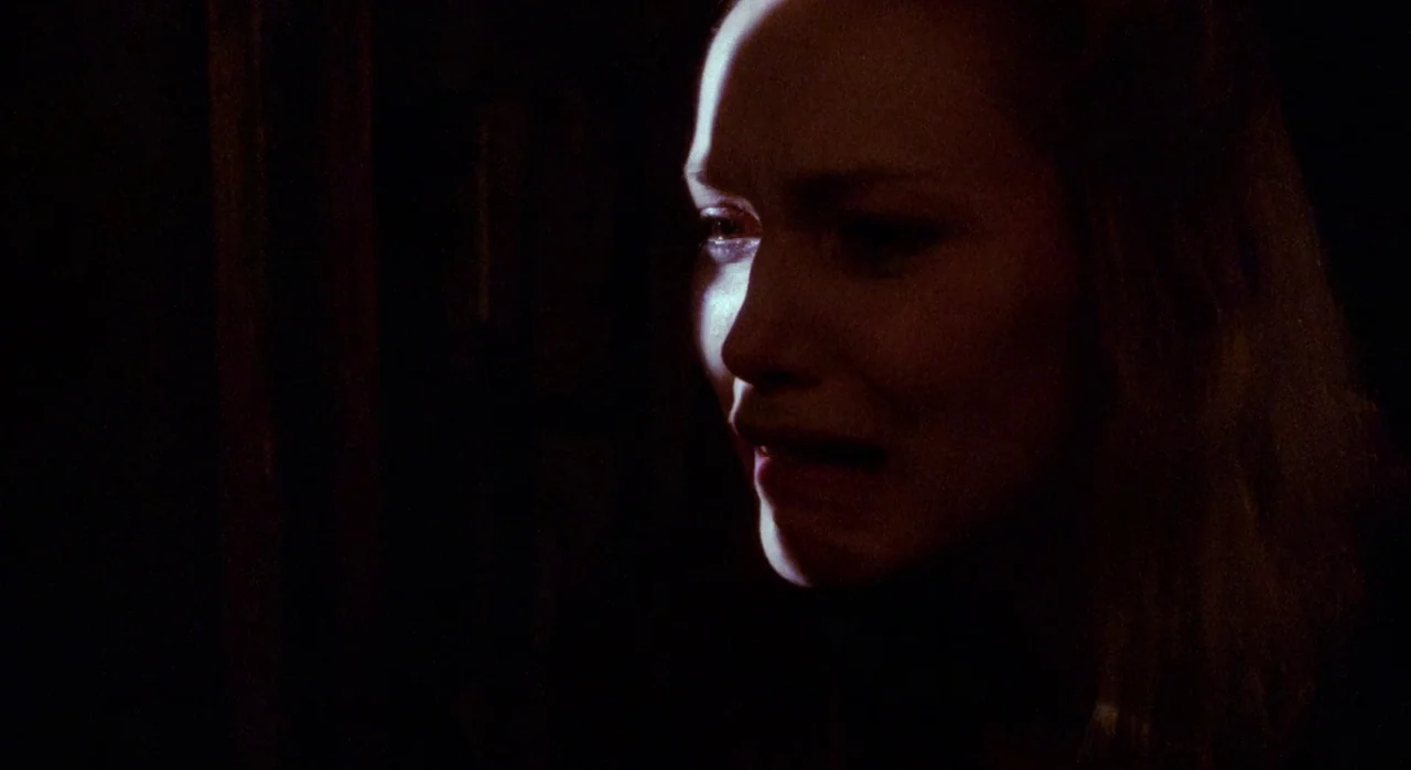 White Of The Eye (1987) movie still: closeup — A dark, undifferentiated interior space with deep black shadows obscuring the surroundings. A young…