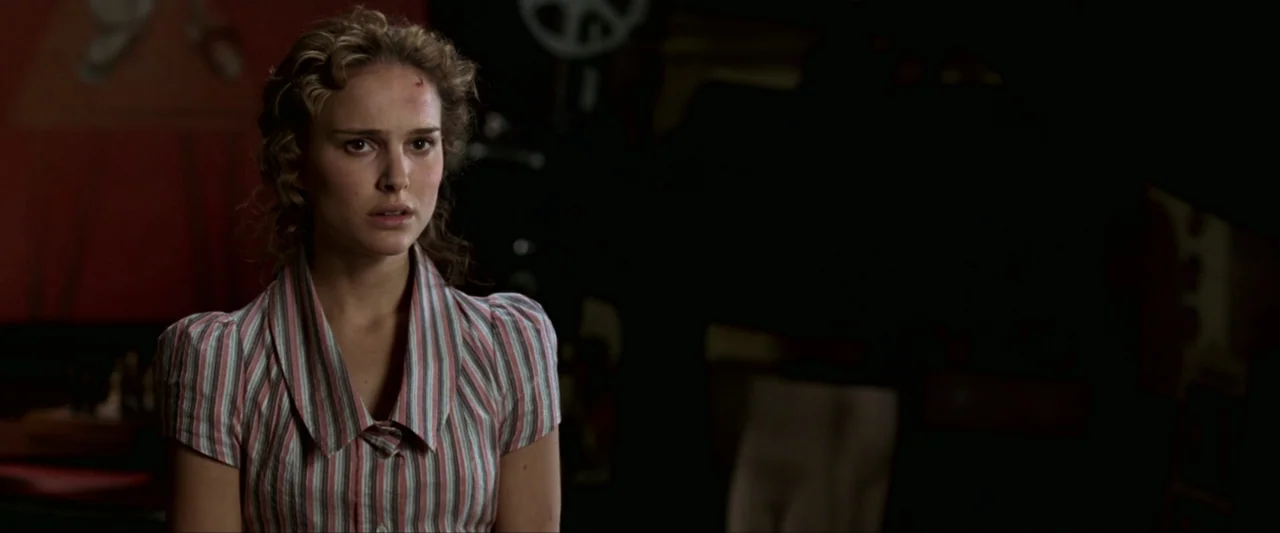 V for Vendetta (2006) movie still: medium — A dimly lit room with vintage film projection equipment visible in the dark background. A young woman…