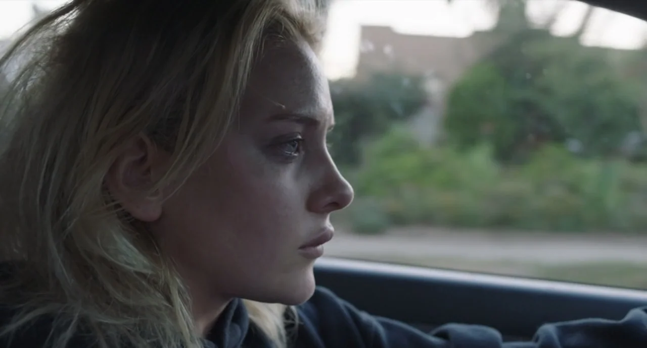 Pleasure (2021) movie still: closeup — A view from inside a car looking across the passenger seat at the driver. The driver focuses on the road as…