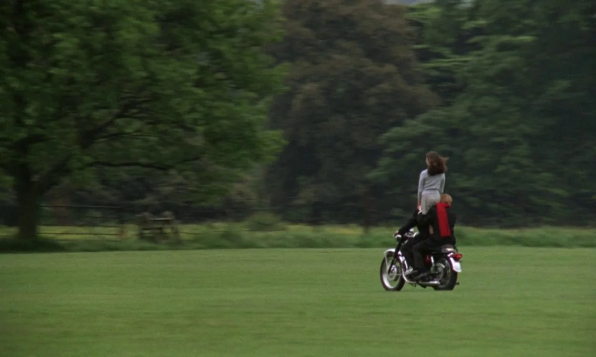 If…. (1968) movie still: wide — A vast green pasture stretches towards a dense line of mature trees. Two people ride a vintage motorcycle across the…