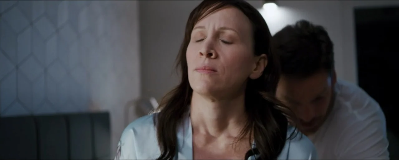 Hostages (2017) movie still: medium — A modern bedroom with a geometric textured wall and a bed headboard. A woman sits with closed eyes while a man…