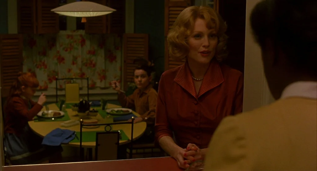 Far From Heaven (2002) movie still: medium — A 1950s-style home interior features a round dining table with patterned floral curtains. A woman…