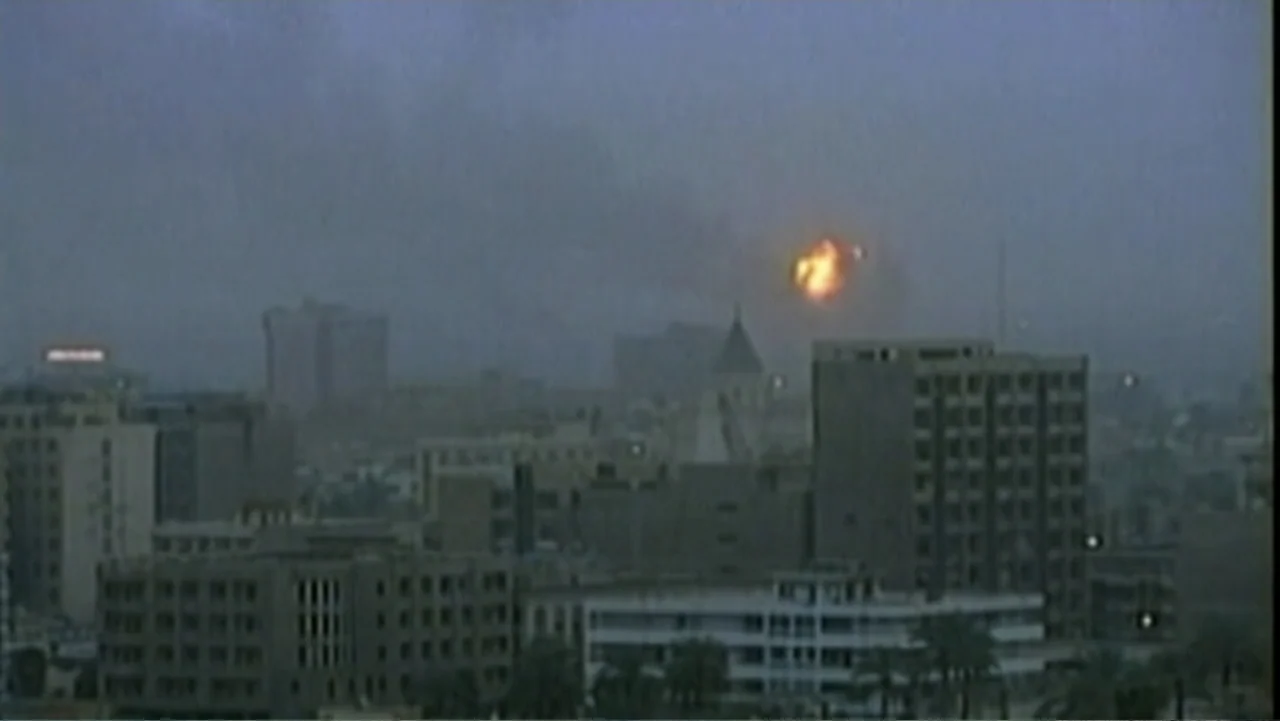 Ghosts of Abu Ghraib (2007) movie still: establishing — A dense urban city skyline is visible under a grey, overcast dusk sky. A bright orange fire…