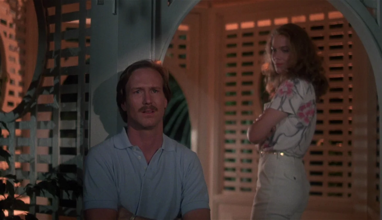 Body Heat (1981) movie still: medium — A white wooden gazebo interior at night features lattice walls and warm lighting. A man stands facing forward…