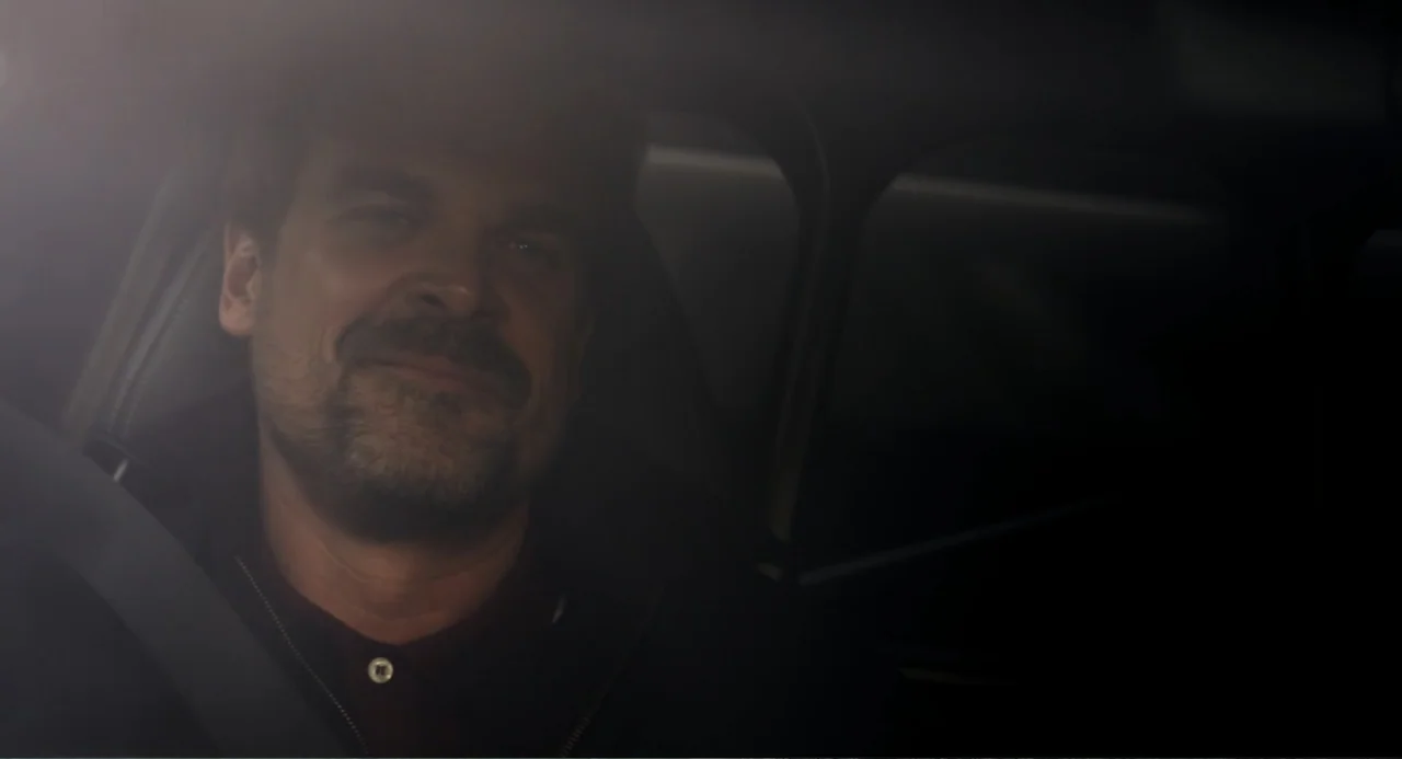 Gran Turismo (2023) movie still: closeup — A dimly lit car interior at night with a man sitting in the driver seat. The man sits behind the steering…