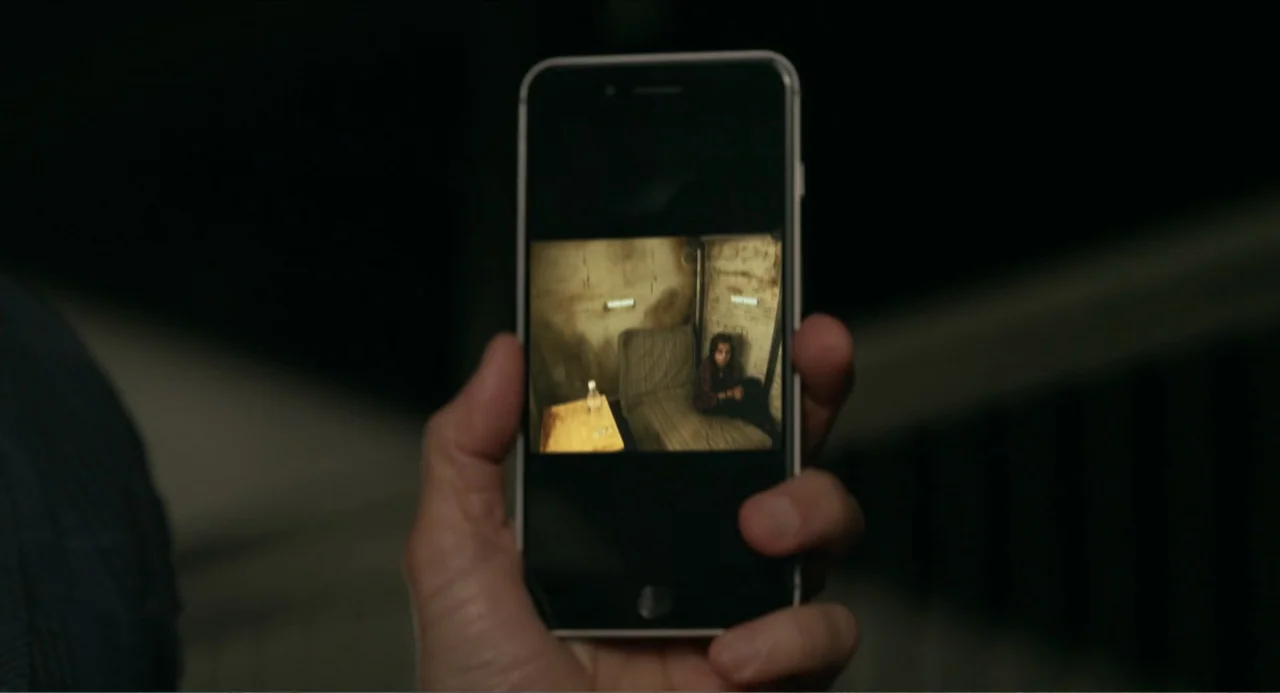 Instantes Capturados (2022) movie still: closeup — A close up view shows a hand holding a modern smartphone in a dark environment. The phone screen…