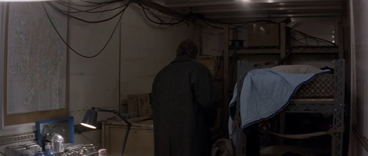 The Russia House (1990) movie still: medium — A dimly lit interior of a cargo trailer contains shelving, cables, and a map. An older man in a long…
