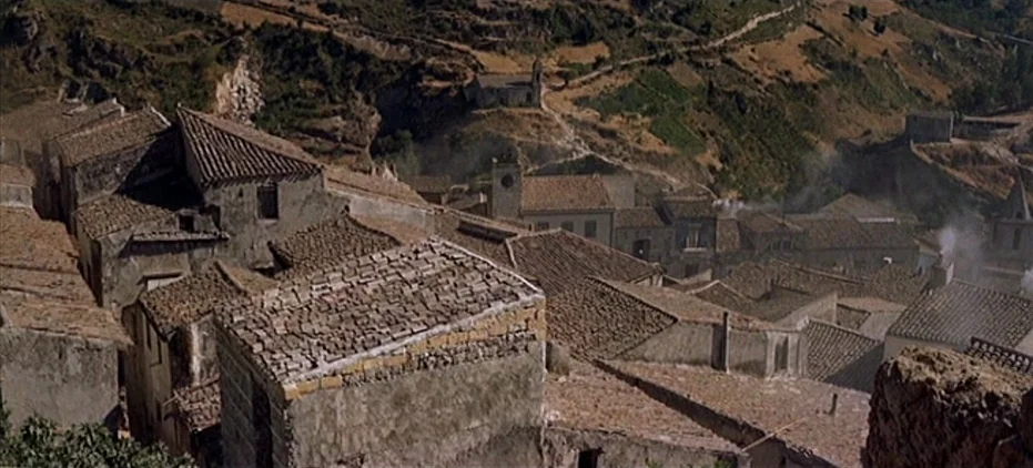 The Leopard (1963) movie still: establishing — An old Italian village with clustered stone houses and terracotta tiled roofs. The structures are…