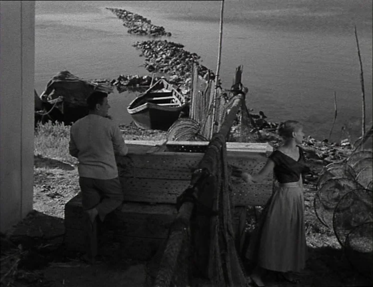 La Pointe Courte (1955) movie still: fullbody — A man and a woman stand by fishing equipment on a wooden dock by water. A small boat is moored…