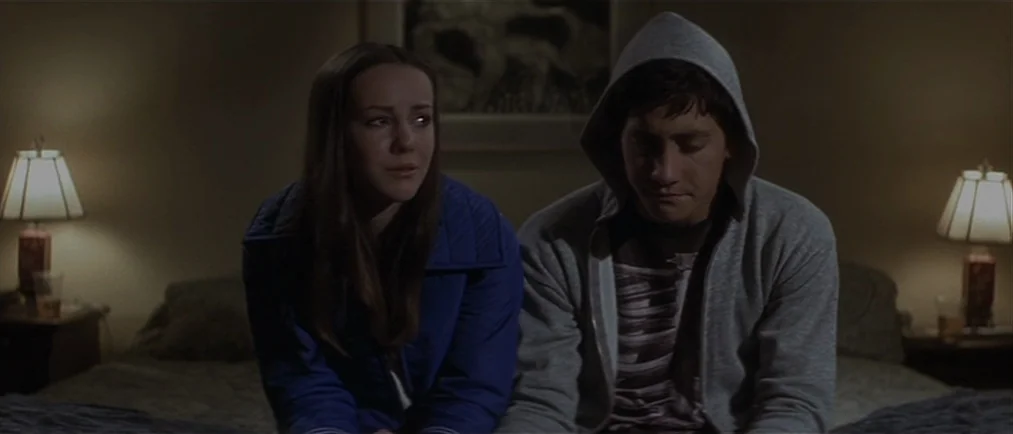 Donnie Darko movie still: medium — Two teenagers sit on a hotel bed in a dim, sparsely decorated space. They sit side by side looking away from each…