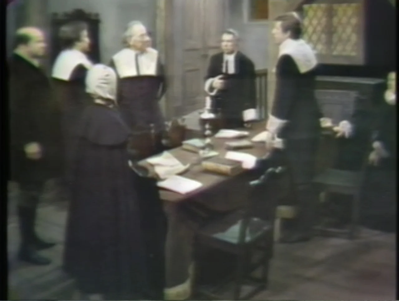 The Crucible (1996) movie still: medium — A dimly lit room with wood paneling contains a large table covered in papers. Several figures dressed in…