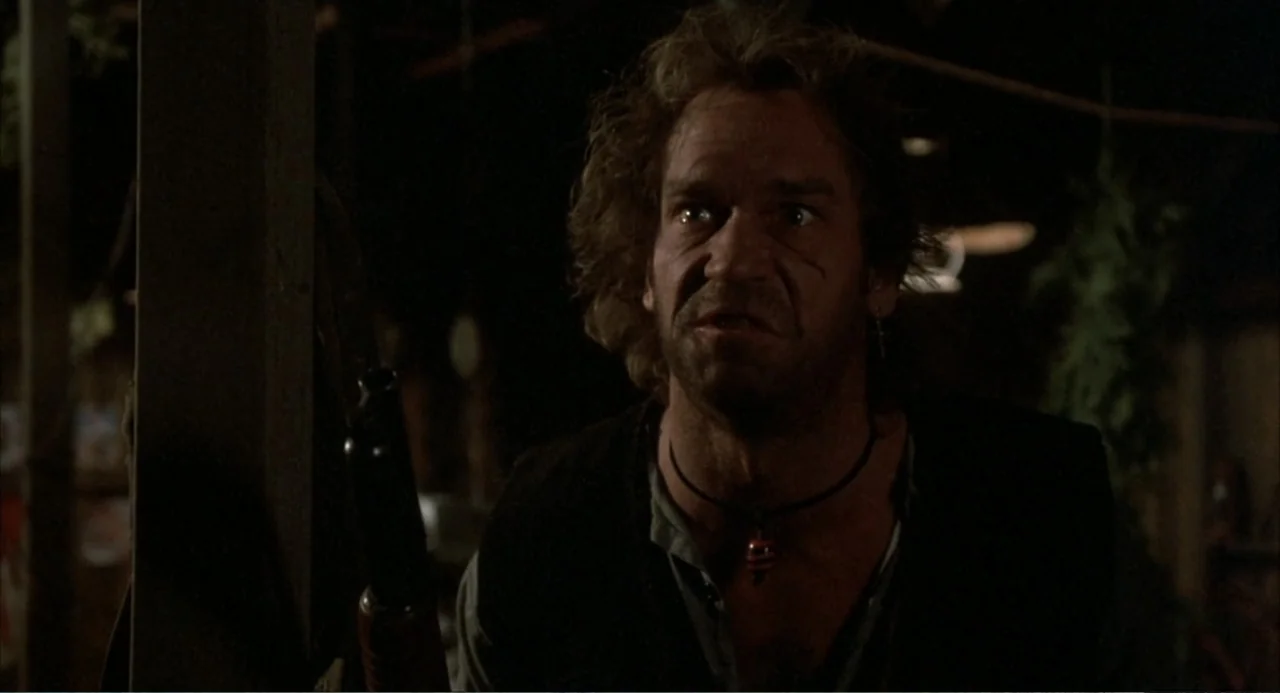 Murphy's Law (2009) movie still: medium — A dimly lit indoor space with blurred background elements and wooden architectural textures. A disheveled…