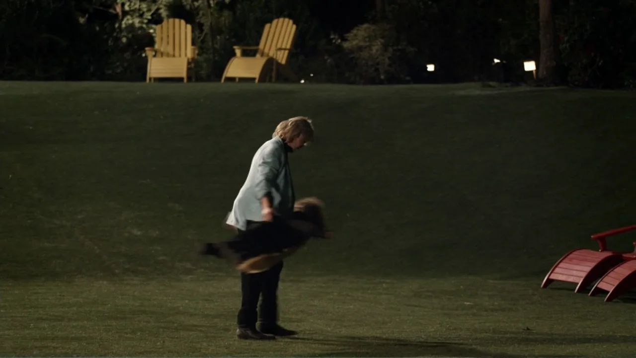 Grown Ups 2 (2013) movie still: wide — A dark, expansive lawn at night featuring pairs of yellow and red lounge chairs. An adult figure stands in…