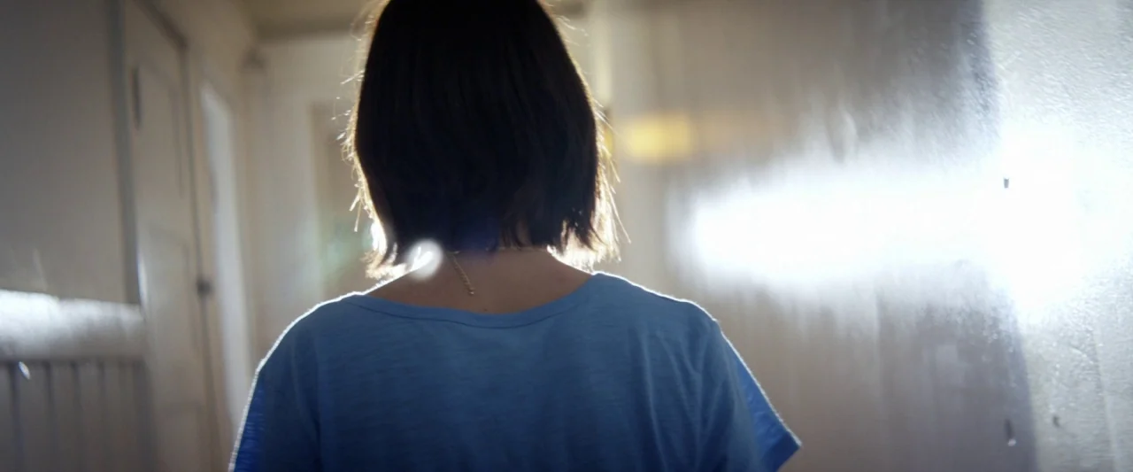 Seven Stages to Achieve Eternal Bliss (2018) movie still: medium — A narrow residential hallway with plain white walls and closed doors on the side.…