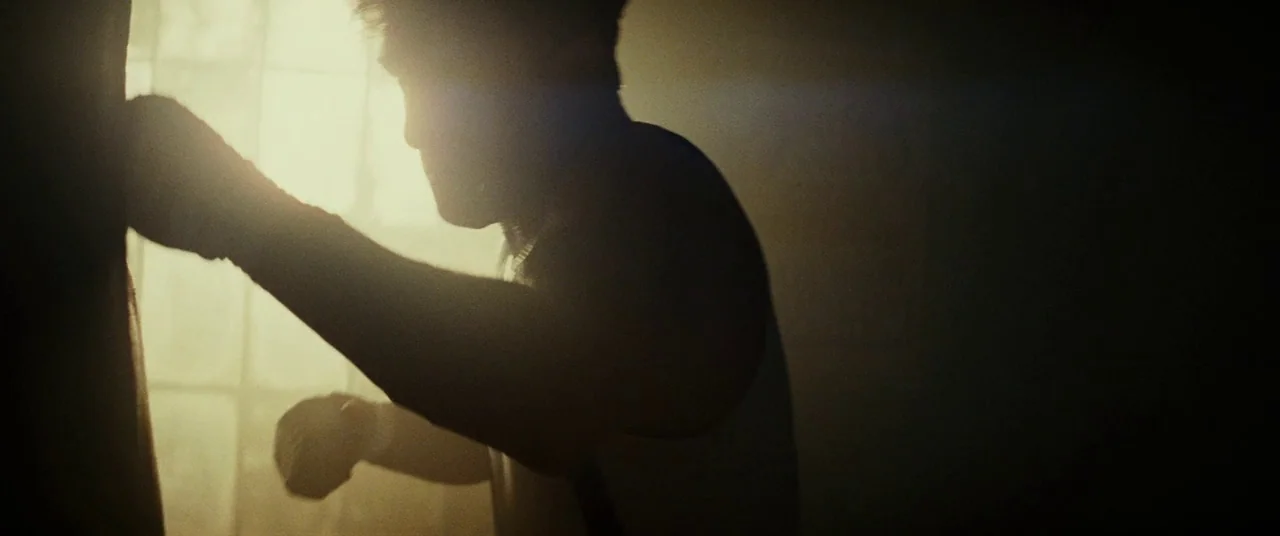 Gangster Squad (2013) movie still: medium — A dimly lit room with bright light spilling through a large, paneled window. An athletic man punches a…
