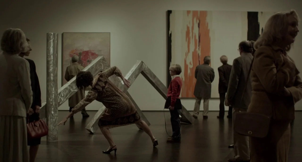 Beginners (2010) movie still: fullbody — A spacious art gallery features large abstract paintings and metallic structural sculptures. A woman in a…