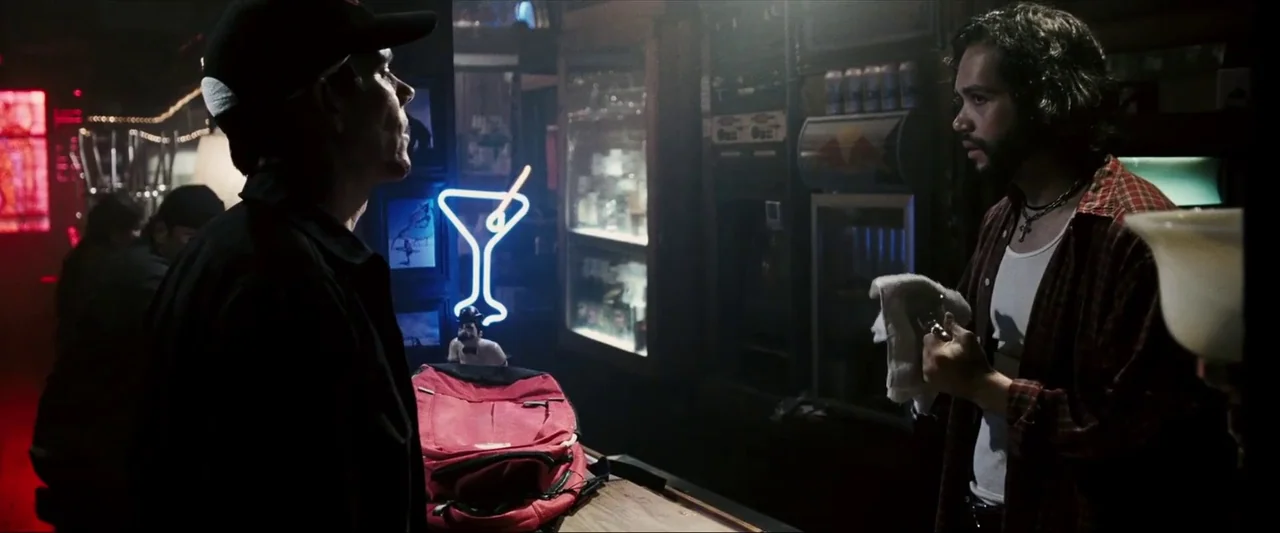 Death Sentence (2007) movie still: medium — A dimly lit bar with a red backpack resting on the wooden counter. Two men face each other across the…