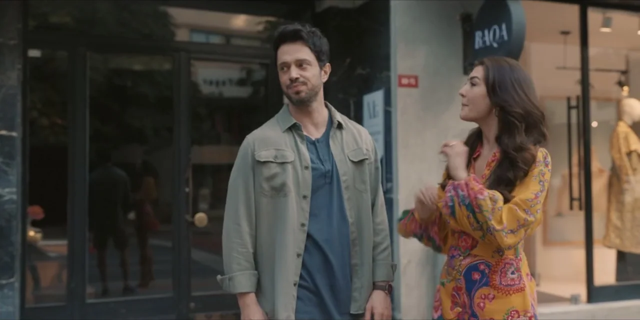 Kill Me If You Dare (2019) movie still: medium — A man and a woman stand on a city sidewalk in front of a store. The man looks toward the woman…
