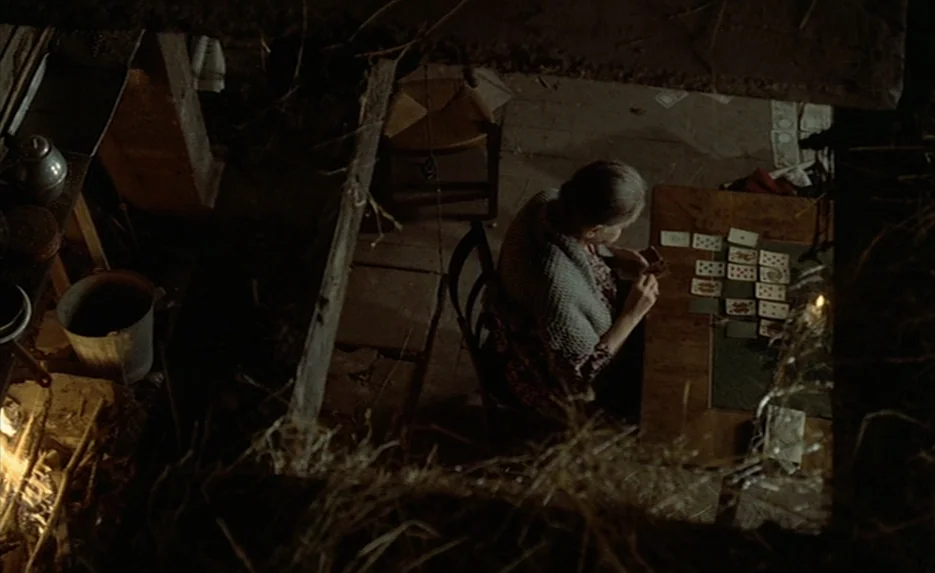 Lacombe, Lucien (1974) movie still: wide — A dimly lit rustic room features a dirt floor covered in dry hay debris. An elderly woman sits at a…
