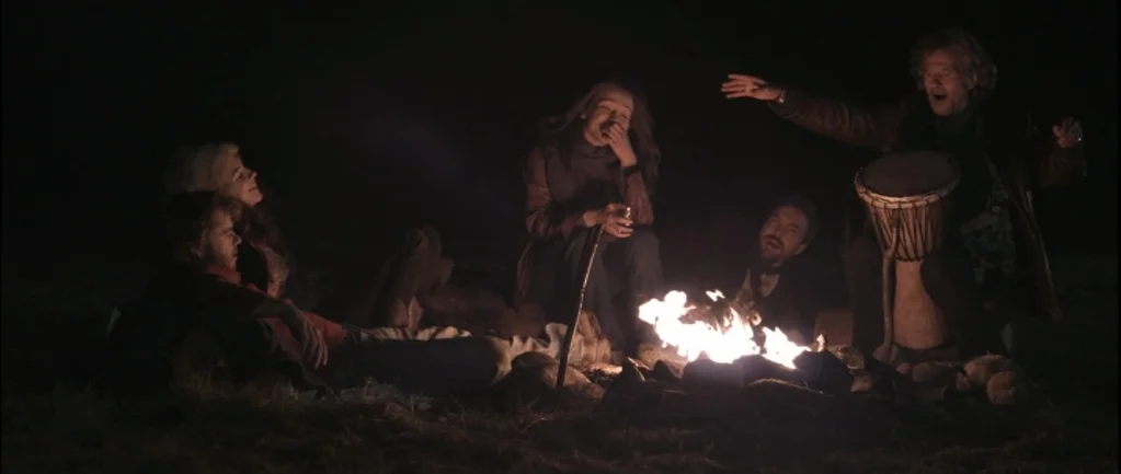One Hundred Mornings (2009) movie still: wide — A group of five individuals sits around a bright fire in a dark outdoor setting. They interact and…