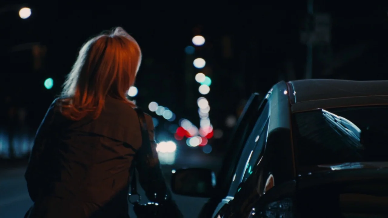 Saw VI movie still: medium — A dark night scene on a city street with blurred out-of-focus traffic lights. A woman with blonde hair stands with her…