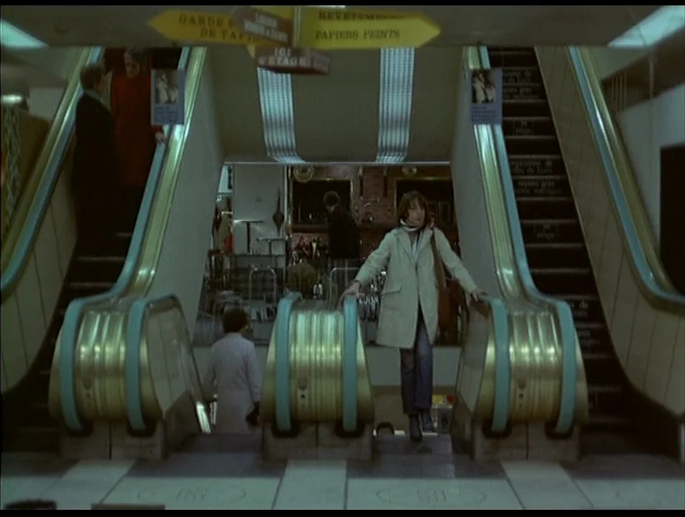 Love In The Afternoon (Chloe In The Afternoon) (L’amour l’après-midi) (1972) movie still: wide — A 1970s department store features dual gold-trimmed…