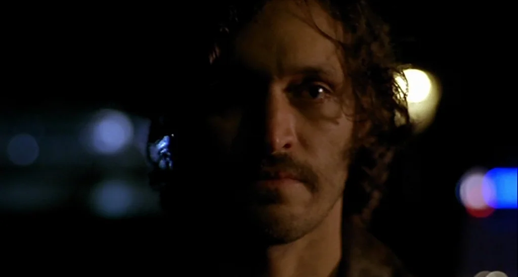 Trouble Every Day (2001) movie still: closeup — A man stands on a dark street at night with out-of-focus city lights behind. The subject looks into…