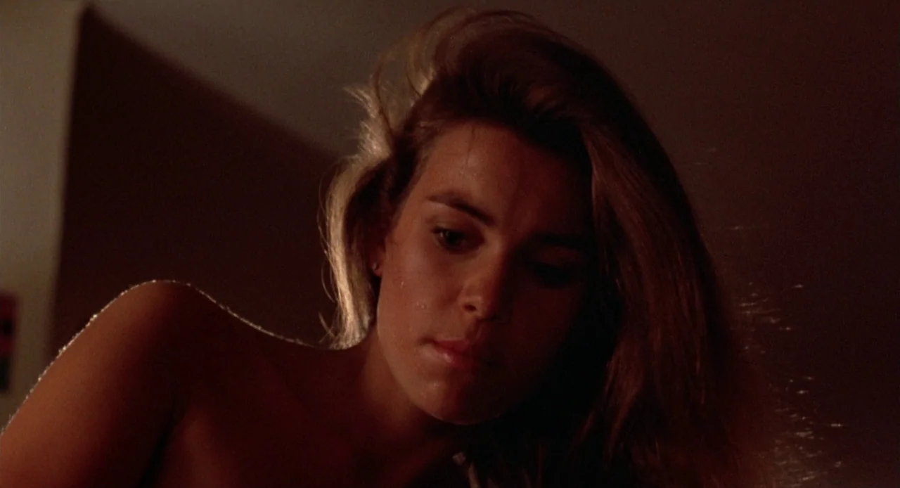 Breathless (1983) movie still: closeup — A dark indoor space with a single light source defining the foreground subject. The subject's hair is…