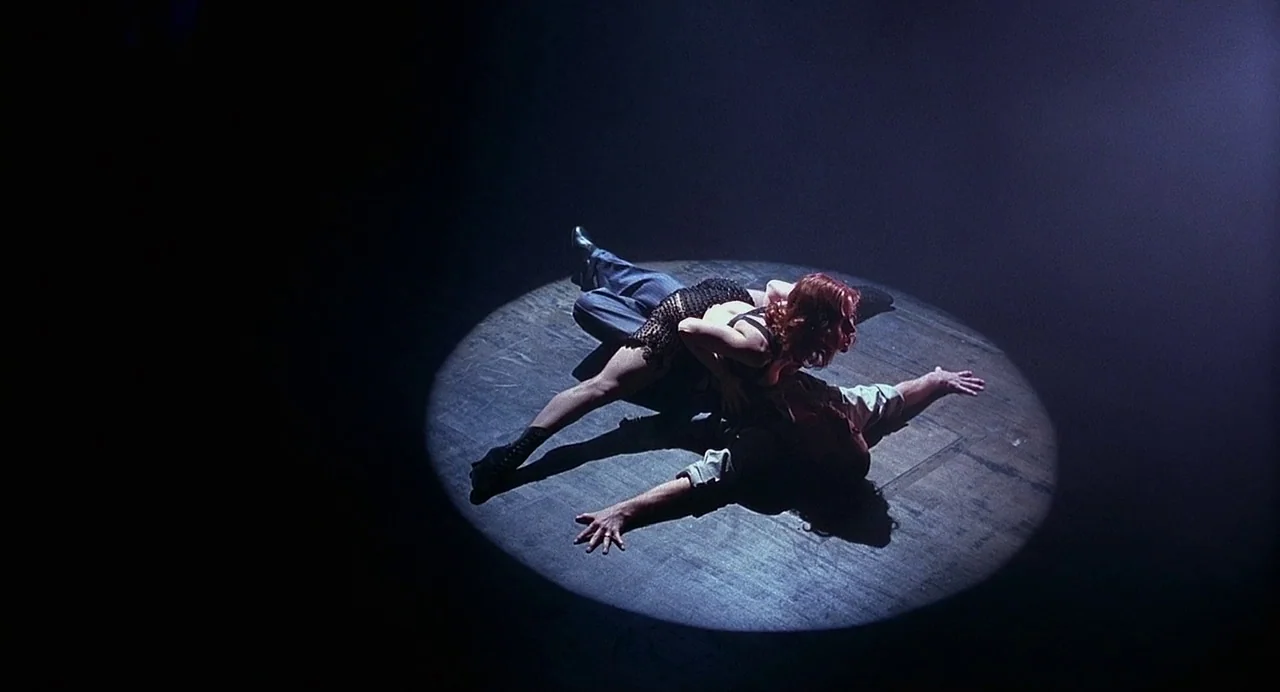 Chicago (2002) movie still: wide — Two people are positioned on a circular wooden floor within a sharp spotlight beam. They are engaged in a…