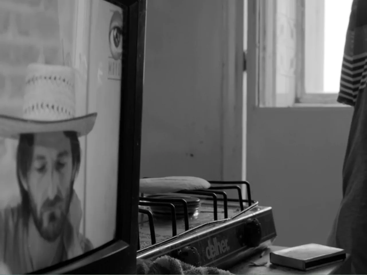 Güeros (2014) movie still: medium — A kitchen counter contains a portable gas stove and a small matchbox. A television screen displays a man wearing…