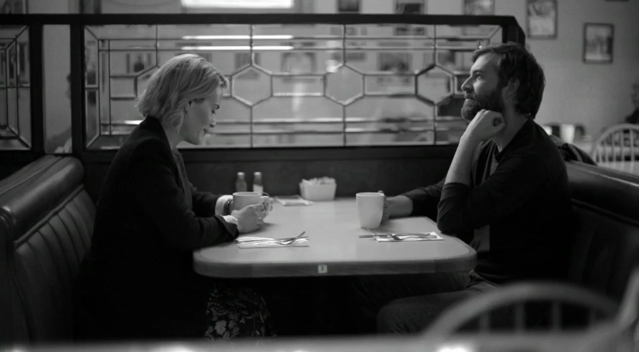 Blue Jay (2016) movie still: medium — A booth in a diner features a leaded glass divider behind the table. A man and a woman sit facing each other…
